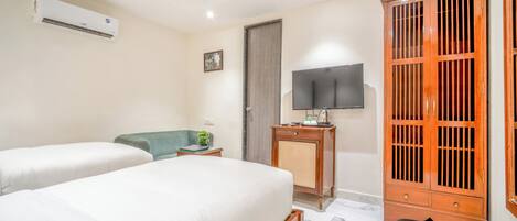 A hotel room with two beds, a television, a wardrobe, and an air conditioning unit.