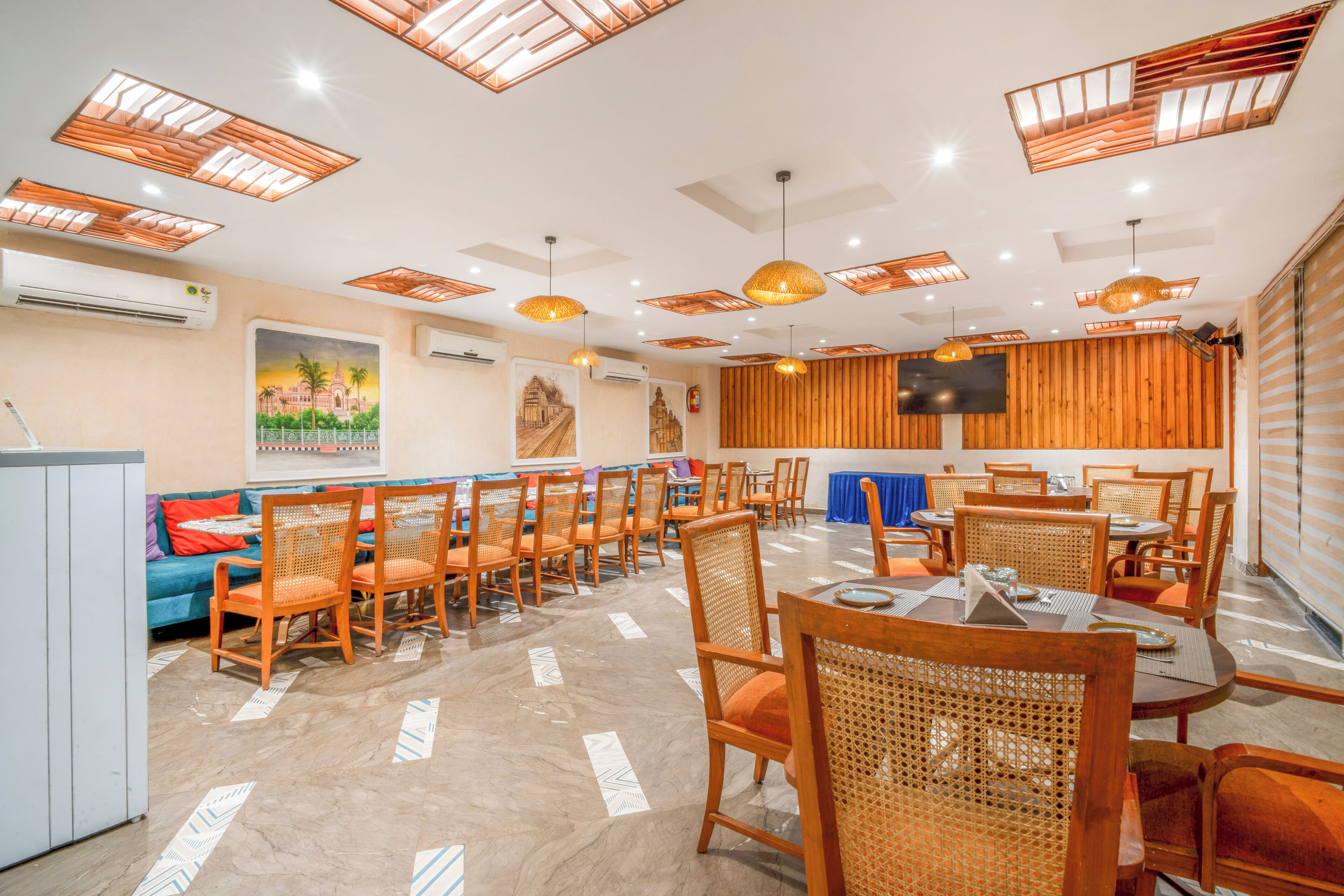 A dining area with wooden chairs and tables, ceiling lights, and a television on the wall.
