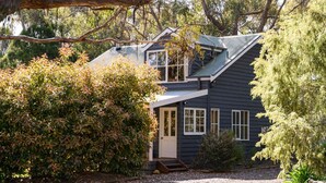 A two-story house with a dark exterior, white trim, and a small front porch. - Ethel Cottage (Drummond)