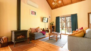 A cozy living room with a fireplace, a sofa, a coffee table, and a television. - Ethel Cottage (Drummond)