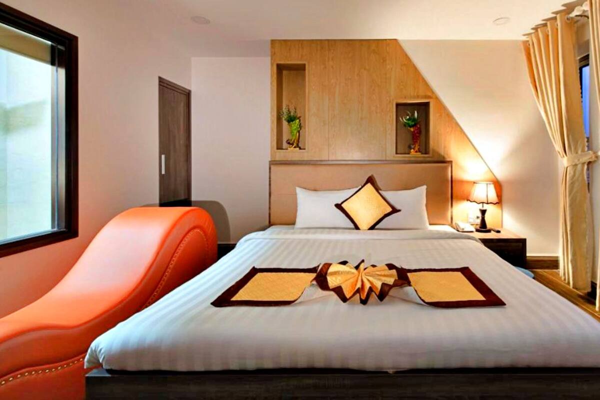 Habitación de hotel con cama, mesita de noche, lámpara, ventana con cortinas y una silla.