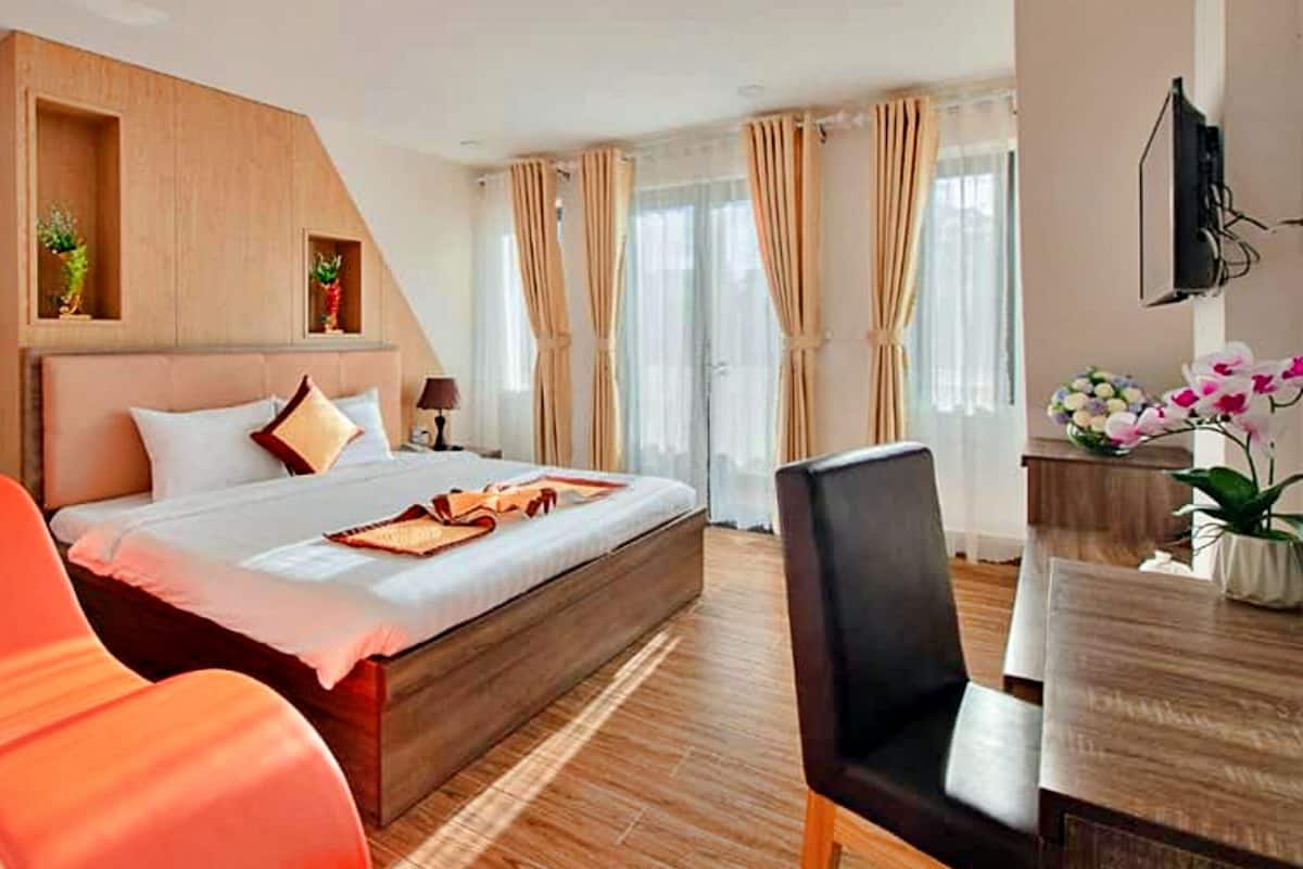 Habitación de hotel con cama, cabecero de madera, escritorio con silla y ventana con cortinas.