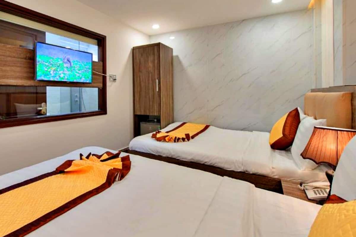 Habitación de hotel con dos camas, un televisor en la pared, un armario de madera y un escritorio con una lámpara.