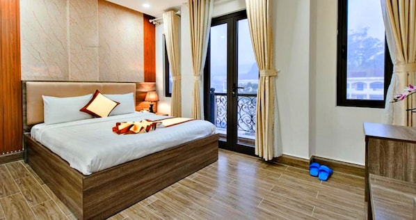 A hotel room with a large bed, a balcony with a view, and a wooden floor.