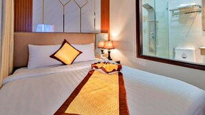 A hotel room with a large bed, a bedside lamp, a window with a view of a bathroom, and a decorative pillow. - HANZ Gia Hoang Hotel Dalat (Cam Ly - Da Lat)