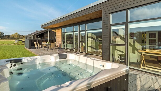 Un espace moderne aménagé à l’extérieur avec un bain à remous, une terrasse en bois, de grandes fenêtres et une vue sur le paysage environnant.