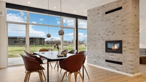 Un espace repas moderne avec une cheminée en briques, de grandes fenêtres et une vue sur l’extérieur.