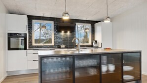 Une cuisine moderne dotée d’un grand îlot central, d’appareils électroménagers en acier inoxydable et offrant une vue agréable par les fenêtres.