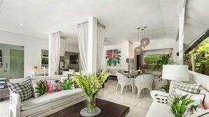 Un salon moderne avec un canapé blanc, une table basse et un coin repas doté de meubles en osier.