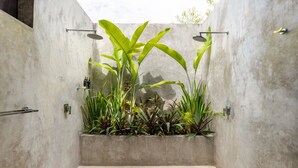 Un espace douche moderne avec un mur en béton, un bac à plantes intégré où sont plantées des plantes tropicales, et une pomme de douche en métal.