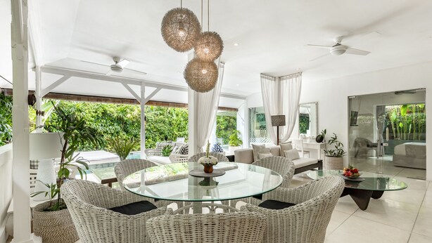 Un salon moderne avec une table basse en verre, des meubles en osier et une vue sur une végétation luxuriante.