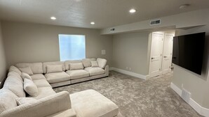 Un salón amplio con un sofá modular grande, un televisor de pantalla plana montado en la pared y suelo alfombrado.