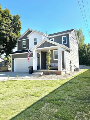 A two-story house with a garage, a small porch, and a flag. - New 4BR Nephi, UT Home - 12 Beds, Game Garage, RV Pad, Near Mt. Nebo & I-15 (Nephi)