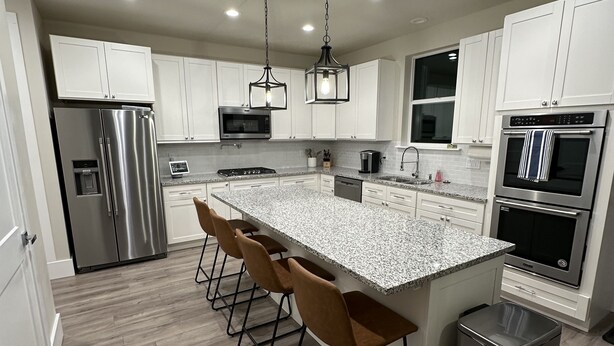 Una cocina moderna con armarios blancos, electrodomésticos de acero inoxidable, encimera de granito y una zona de bar con taburetes.