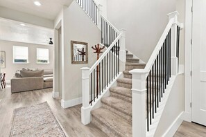 A staircase with white railings and a wooden handrail, leading to a landing with a framed picture and a coat rack. - New 4BR Nephi, UT Home - 12 Beds, Game Garage, RV Pad, Near Mt. Nebo & I-15 (Nephi)