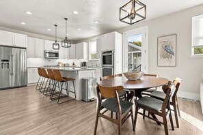 A modern kitchen with white cabinets, stainless steel appliances, and a dining area with wooden chairs and a round table. - New 4BR Nephi, UT Home - 12 Beds, Game Garage, RV Pad, Near Mt. Nebo & I-15 (Nephi)
