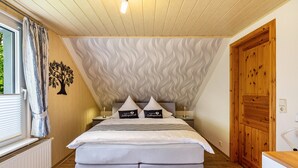 A bedroom with a bed, a window with curtains, a radiator, a wooden door, and a wall with a wavy pattern. - Apartment 'Ferienwohnung Lucke' with Mountain View, Private Terrace and Wi-Fi (Oybin-Luftkurort Lückendorf)