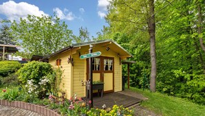 A yellow cabin with a wooden deck, surrounded by lush greenery and a variety of flowers. - Apartment 'Ferienwohnung Lucke' with Mountain View, Private Terrace and Wi-Fi (Oybin-Luftkurort Lückendorf)