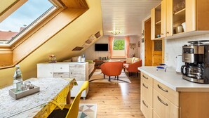 A modern kitchen with wooden cabinets, a coffee machine, and a dining area with a table and chairs. - Apartment 'Ferienwohnung Lucke' with Mountain View, Private Terrace and Wi-Fi (Oybin-Luftkurort Lückendorf)