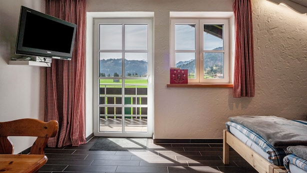 Une chambre avec un lit, une télévision, une fenêtre avec des rideaux et une vue sur un paysage verdoyant.