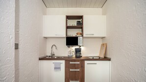 Une cuisine compacte avec des meubles blancs, un plan de travail en bois, un four à micro-ondes encastré, une machine à café et un évier.