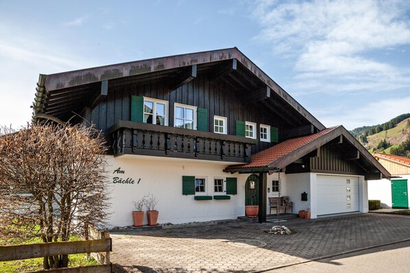 A traditional chalet with a white facade, green shutters, and a wooden balcony.