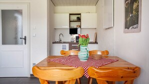 Un coin repas avec une table en bois, des chaises, un vase de fleurs et, au fond, une cuisine.