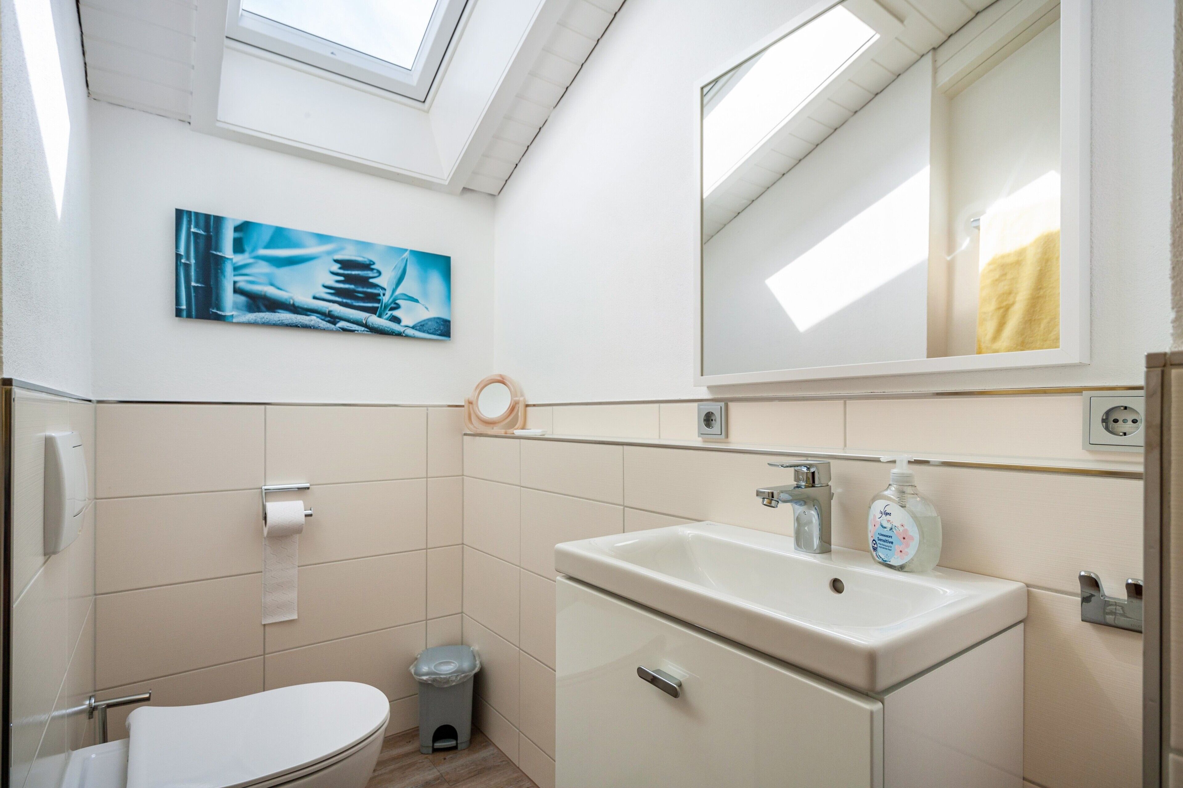 Un baño con tragaluz, un lavabo, un inodoro y un pequeño cubo de basura.