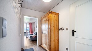 Un couloir avec une armoire en bois, une porte blanche et une vue sur un espace de vie comprenant un canapé et un rideau rouge.