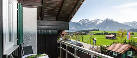 A balcony with a table and chairs, a view of a mountain range, and a small building in the distance.