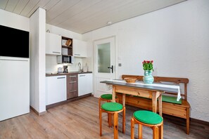 Une cuisine avec des meubles en bois, un four à micro-ondes, un évier et un coin repas comprenant une table en bois et des chaises vertes.