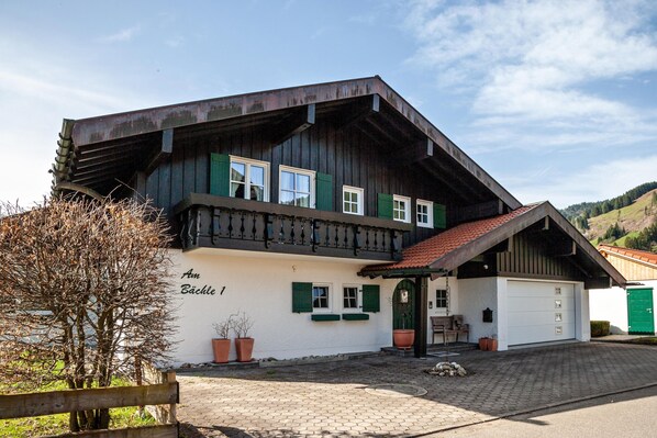 Un bâtiment à deux étages, doté d’une façade blanche, de volets verts et d’un toit recouvert de tuiles rouges.