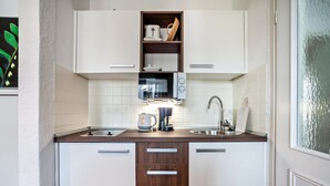 A compact kitchen with white cabinets, a microwave, a kettle, and a sink. - Studio Apartment 'Appartement  Braun 3' with Mountain View, Balcony and Wi-Fi (Bolsterlang)