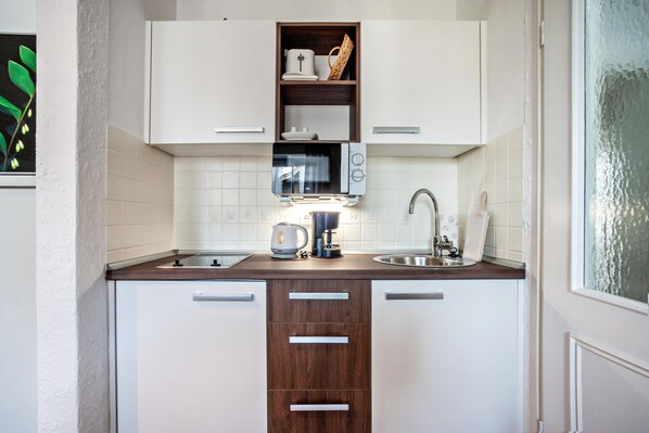 A compact kitchen with white cabinets, a microwave, a kettle, and a sink.
