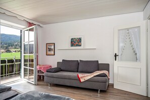 Un salon avec un canapé gris, une table recouverte d’une nappe à carreaux rouges et blancs, un tableau encadré accroché au mur et une porte ornée d’un vitrail décoratif.