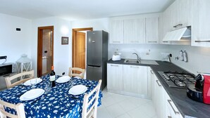 A compact kitchen with white cabinets, a black countertop, and a dining area with a blue tablecloth.