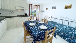A compact kitchen with white cabinets, a dining table set with plates and glasses, and a bed with a blue patterned bedspread.