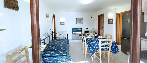 Un espace repas comprenant une longue table et des chaises, un téléviseur et un réfrigérateur.