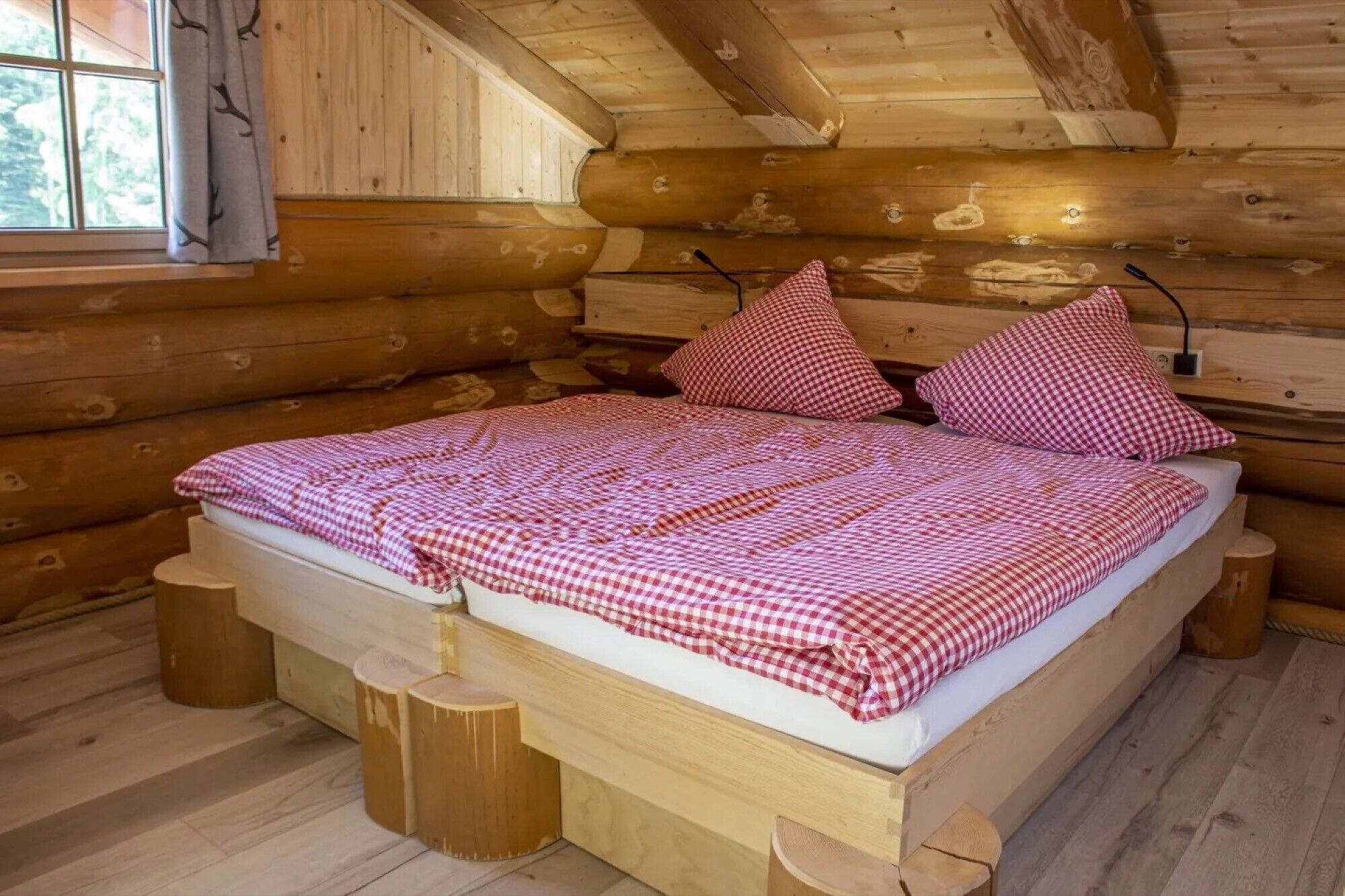 Ein Schlafzimmer einer Holzhütte mit einem Bett, karierter Bettwäsche und einem Fenster mit Vorhängen.