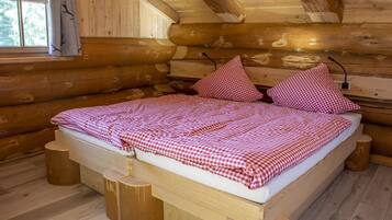 Ein Schlafzimmer einer Holzhütte mit einem Bett, karierter Bettwäsche und einem Fenster mit Vorhängen.