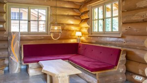 L’intérieur d’une cabane en rondins, avec un banc en bois, un coin salon avec des coussins et deux fenêtres.