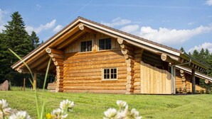 Une cabane en rondins avec un toit à deux versants, une fenêtre centrale et une porte de garage.