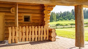 Une cabane en rondins avec un porche en bois, une fenêtre et une vue sur un paysage verdoyant.