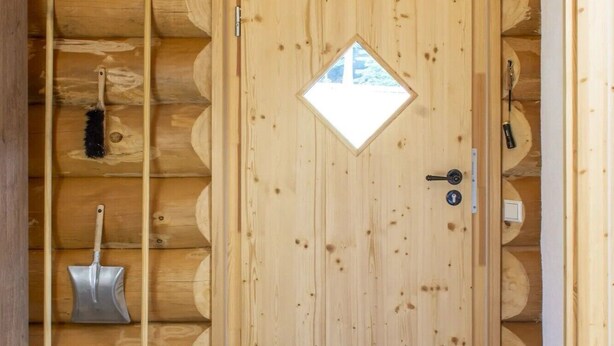 L’intérieur d’une cabane en rondins, avec une porte en bois, une petite fenêtre et un paillasson.