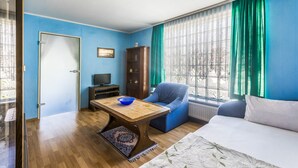 Una habitación con una mesa de madera, una silla azul, un sofá, un armario y una ventana con cortinas.