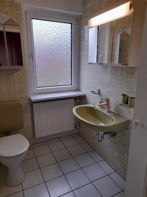 Une salle de bain avec des toilettes, un lavabo, une fenêtre et un miroir.