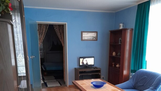 Ein Zimmer mit einem Bett, einem Sofa, einem Tisch mit einer Schale, einem Fernseher, einem Schrank und einer Tür zu einem weiteren Raum.
