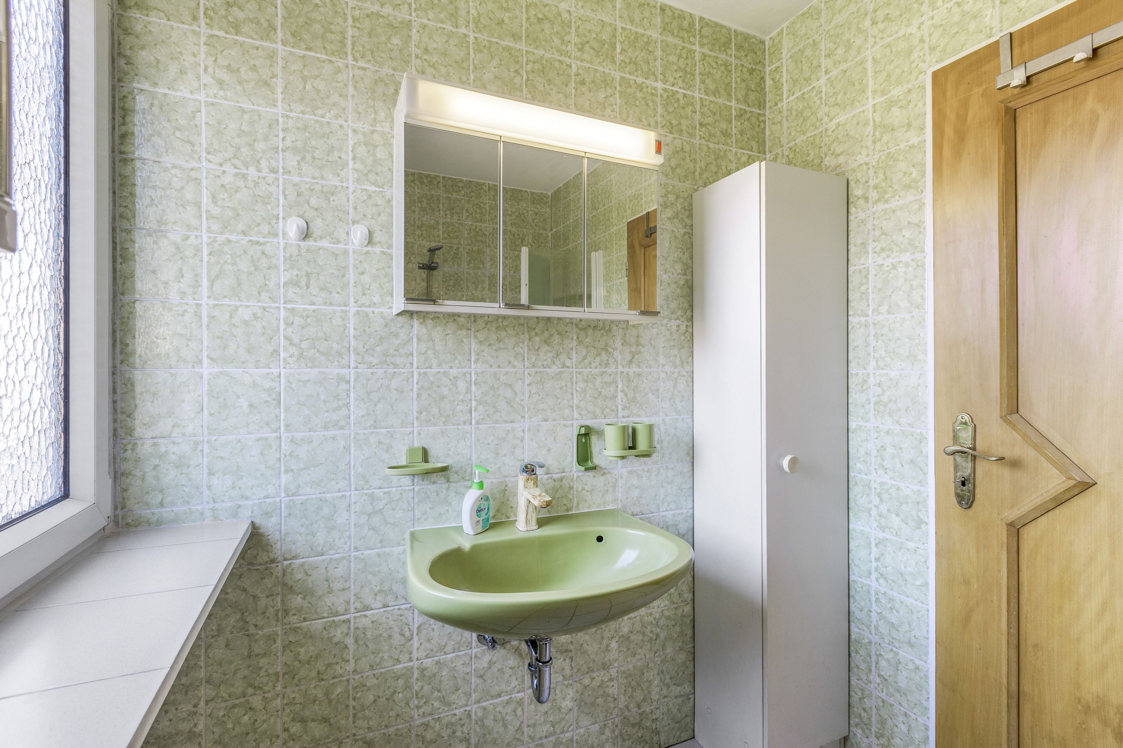 Een badkamer met een groene wastafel, een spiegel erboven en een houten deur.