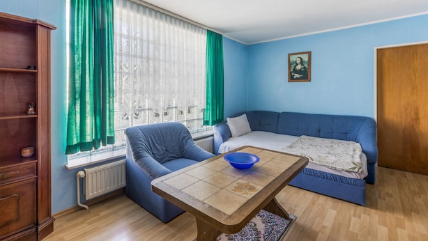 Una habitación con un sofá azul, una mesa de madera, un radiador y una ventana con cortinas verdes.