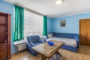Una habitación con un sofá azul, una mesa de madera, un radiador y una ventana con cortinas verdes.